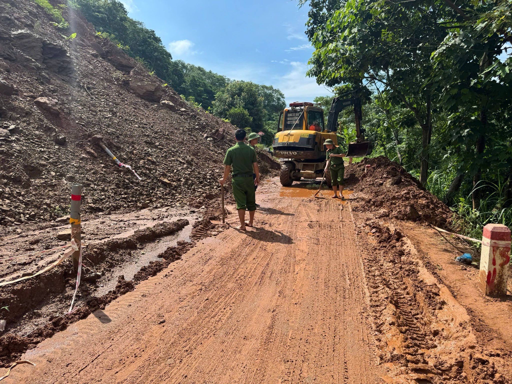 Lực lượng chức năng phối hợp sử dụng cuốc, xẻng và máy múc khẩn trương dọn sạch đất đá sạt lở, đảm bảo an toàn và thông suốt cho tuyến đường sau mưa lớn. Ảnh : An Ninh Lào Cai