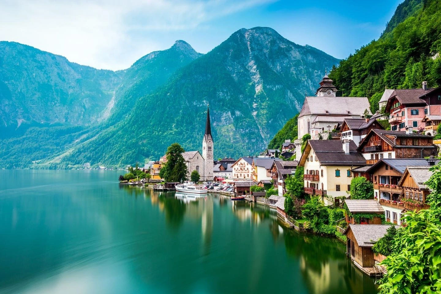 Tựa lưng vào triền núi xanh ngát, bên hồ Hallstatt trong vắt như gương, ngôi làng nhỏ của nước Áo hiện lên như cảnh sắc trong chuyện thần tiên. Những ngôi nhà gỗ cổ kính vững chãi trên sườn núi, ban công phủ kín hoa phong lữ đỏ rực, tạo nên bức tranh vừa lãng mạn vừa cổ kính.