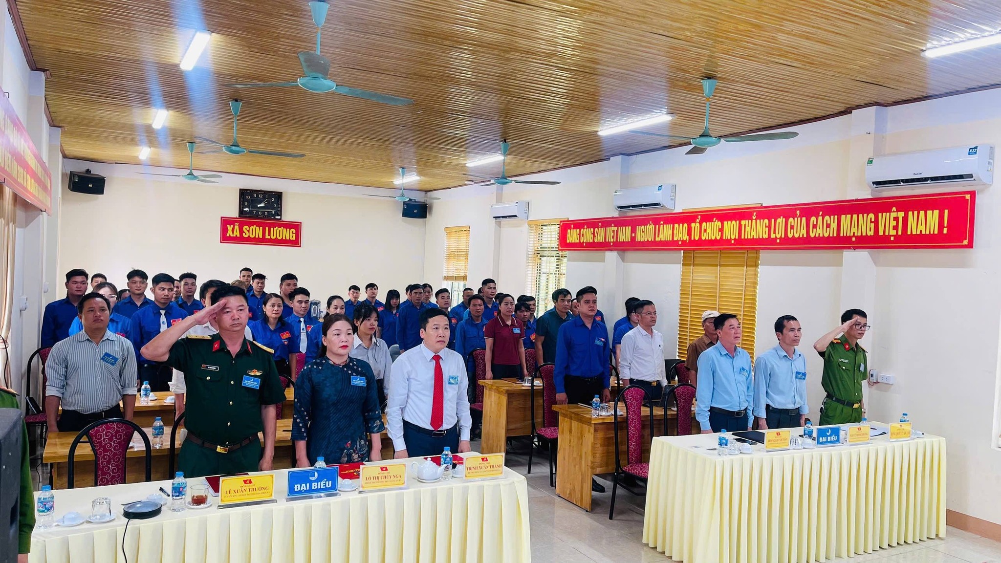 Các đại biểu trang nghiêm đứng dậy, hướng về Quốc kỳ, thực hiện nghi thức chào cờ trong lễ khai mạc đại hội. Không khí buổi lễ diễn ra nghiêm túc, thể hiện tinh thần đoàn kết, trách nhiệm và sự tôn nghiêm của sự kiện.